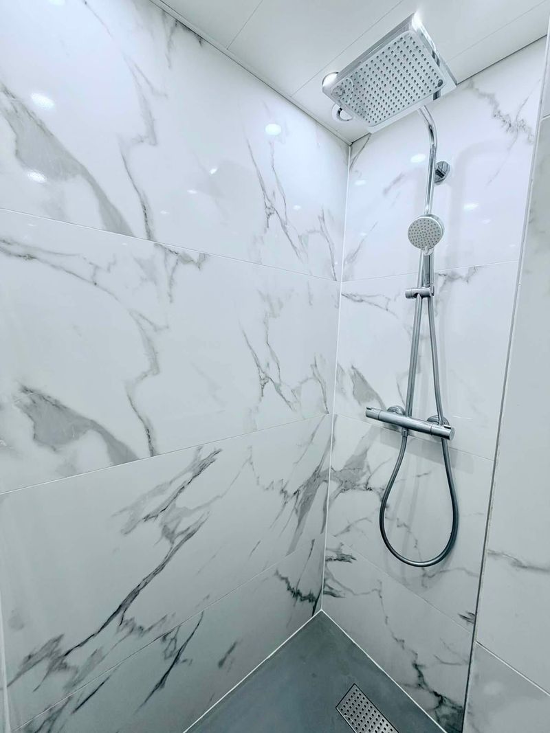 Douche avec colonne thermostatique et pomme de pluie, murs en carrelage effet marbre