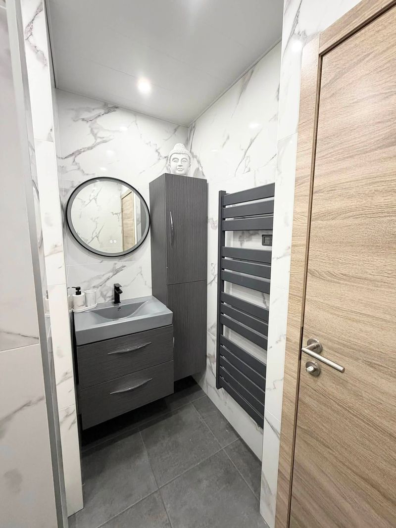 Vasque suspendue grise, miroir rond et sèche-serviettes dans une salle de bain en carrelage effet marbre